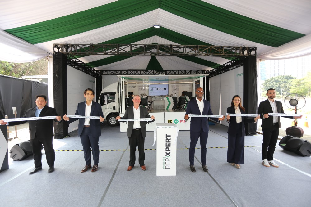 Six people in formal attire stand in a row under a white and green tent for a ribbon-cutting ceremony, holding a ribbon that reads "Schaeffler."